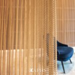 Gold metal coil drapery curtain used as a room divider in a hotel lounge — coiled wire mesh by KAPHS, Dubai & UAE
