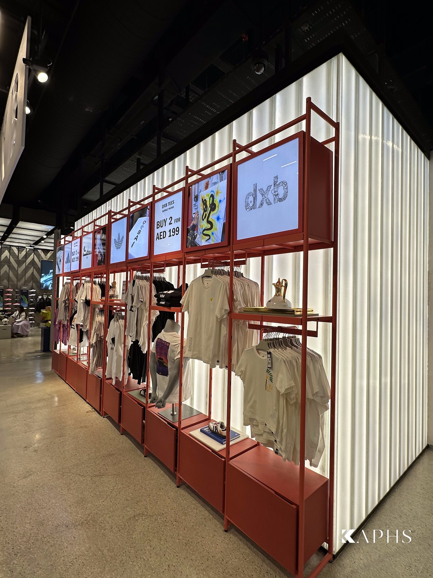DXB tees display against the backlit U-channel glass wall, adidas Flagship Store Dubai Mall — KAPHS