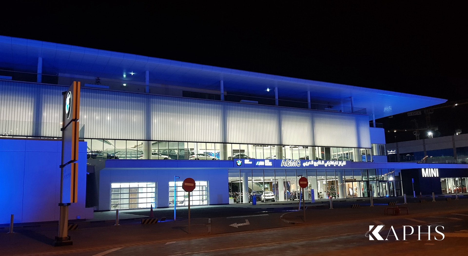 AGMC BMW showroom, Motor City Dubai at night — blue-lit LINIT U-channel glass fascia, KAPHS