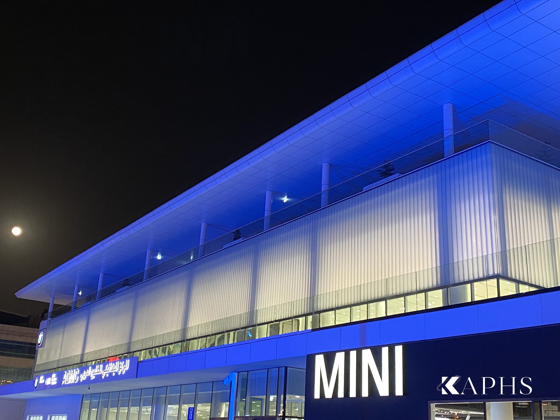 AGMC BMW & MINI showroom, Motor City Dubai — night exterior with channel glass façade, KAPHS