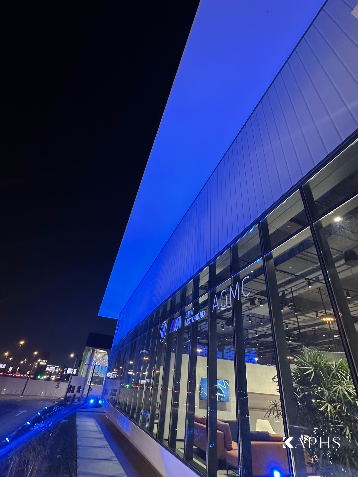 AGMC BMW Motorrad showroom, Sharjah — blue-lit U-channel glass façade band above the glazed frontage, KAPHS