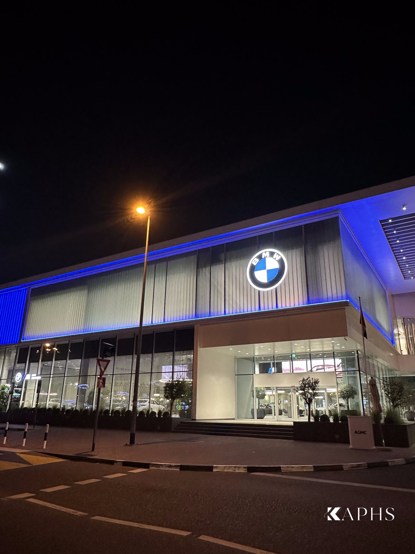 AGMC BMW showroom, Sheikh Zayed Road — night corner elevation with blue-lit U-channel glass façade and main entrance, KAPHS